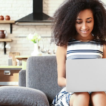 A woman on a couch using a laptop with a dog beside her