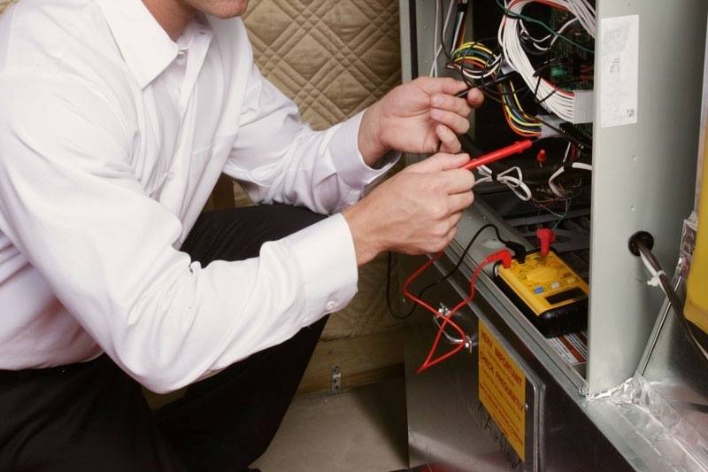 Male HVAC technician kneeling in front of a furnace, performing a repair.