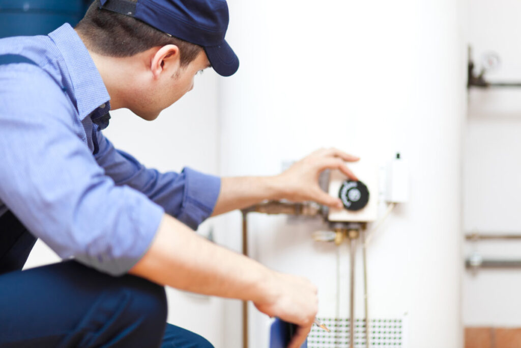 Male plumber adjusting a knob on a water heater.