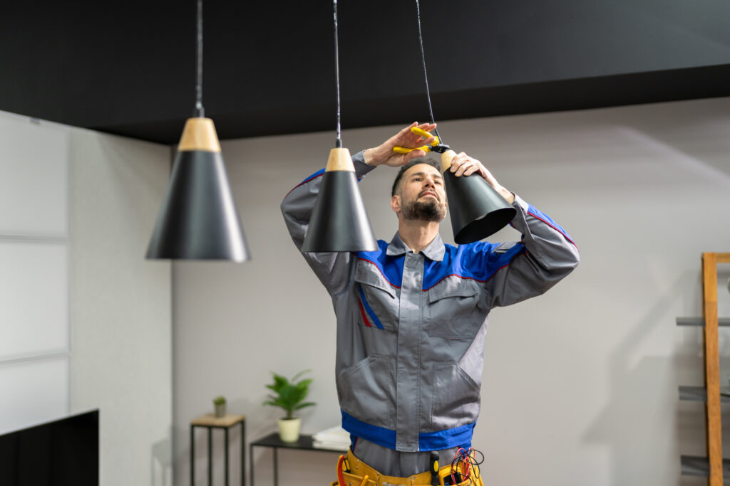 Male electrician installing a pendant light in a residential kitchen.